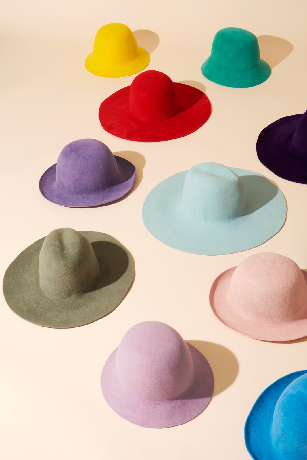 A collection of various colored hats displayed on a white background, including beige, black, blue, green, purple, red, and yellow.