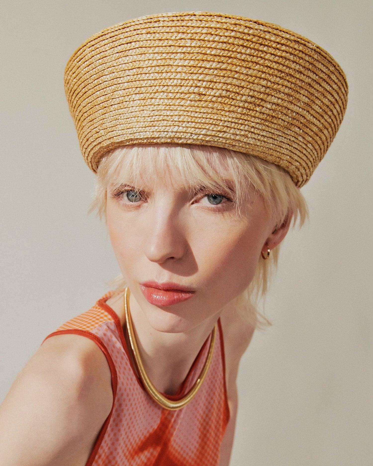 Woman wearing a straw hat and orange dress against a plain background