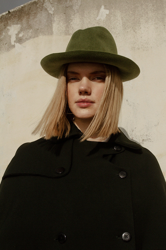 A woman wearing green fedora hat with a curved brim and center-dent crown.