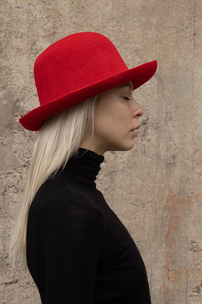 A prson wearing red felt hat with a soft, curved brim and a round crown, paired with black turtle-neck knitblouse.