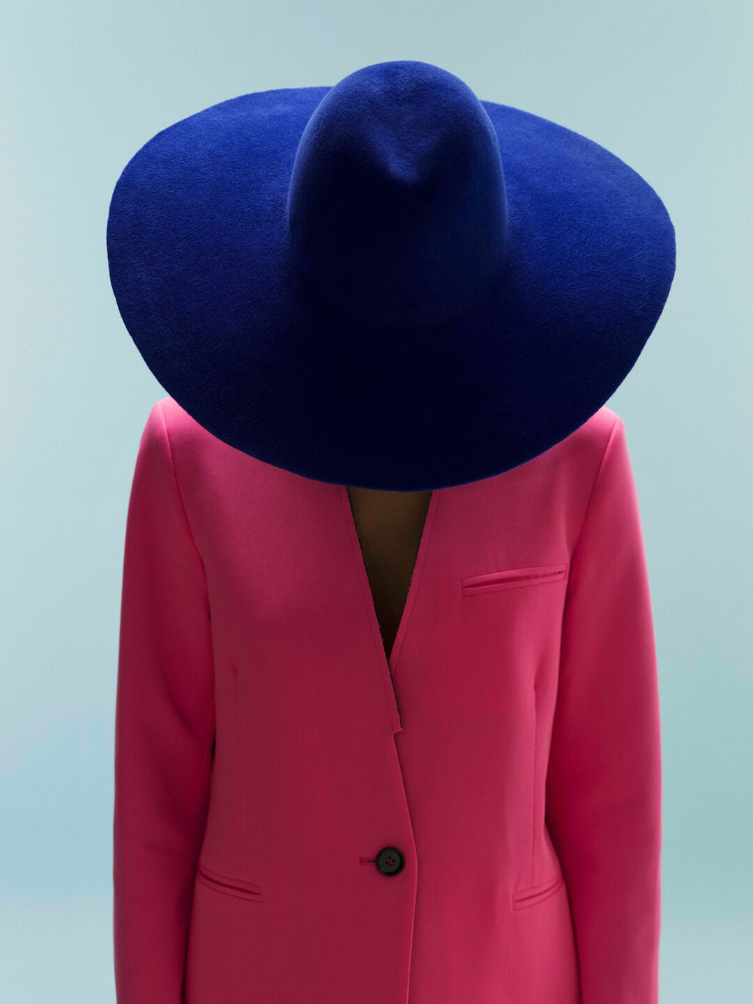 A person wearing a wide-brimmed blue fedora hat with a pink jacket.
